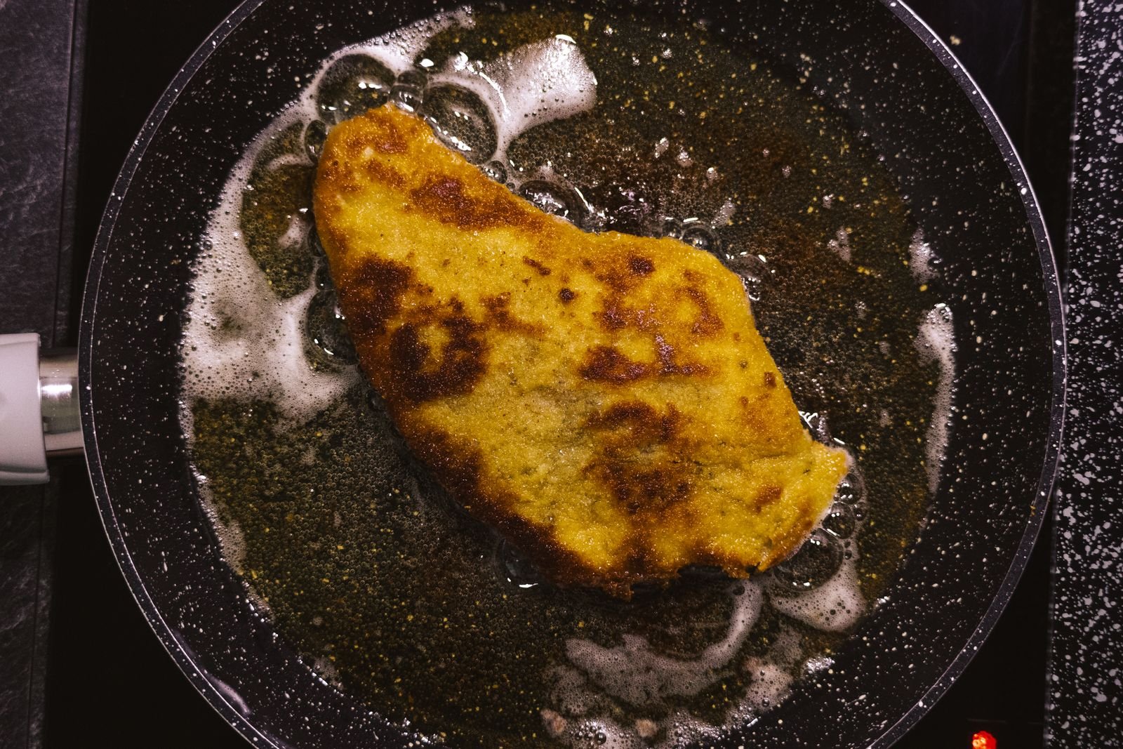 Breaded schnitzel frying in hot fat in a dark pan